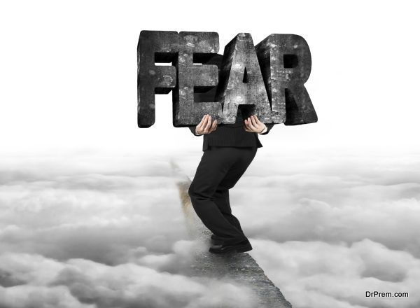 Man carrying big 3D fear concrete word balancing on ridge with with gray cloudy sky background