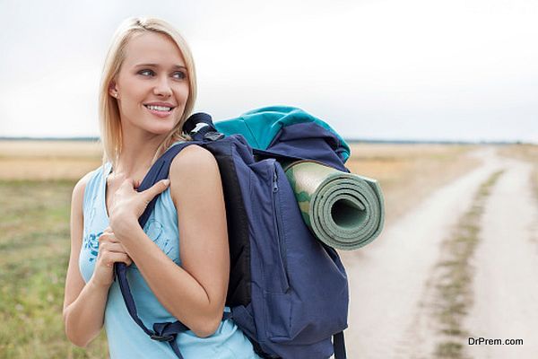 Beautiful woman with backpack looking away while hiking at field