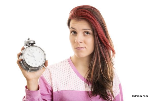 There, I overslept again. What can I do? Young girl in pyjamas holding an alarm clock isolated on white background