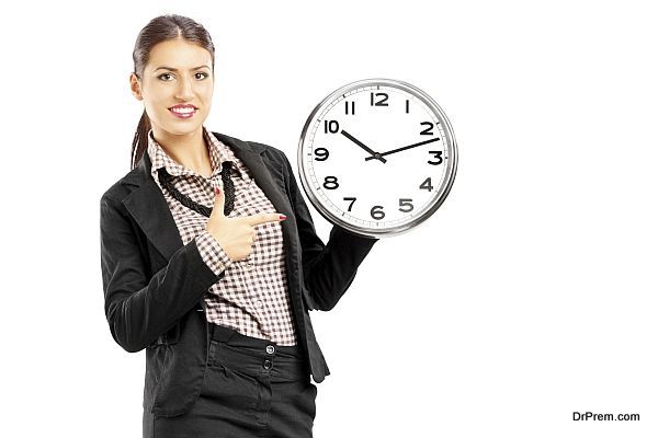 Smiling female standing and pointing on a wall clock, isolated on white background