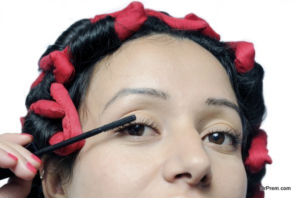 Young Indian girl applying mascara on eyelashes.