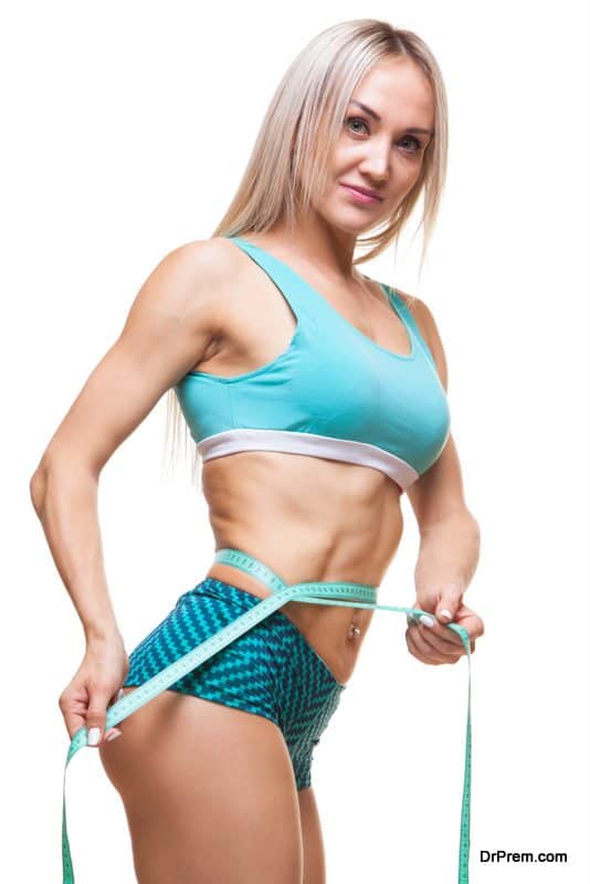 Athletic slim woman measuring her waist by measure tape after a diet over black background