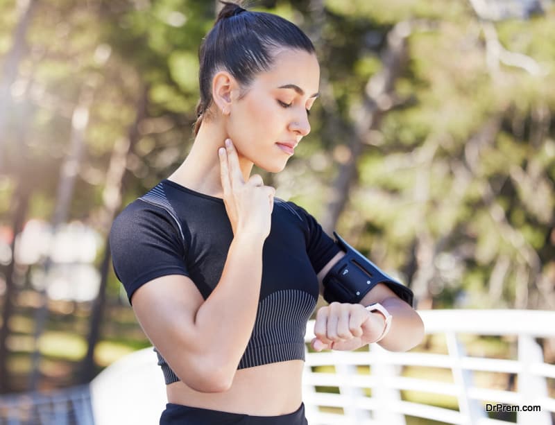 Young sportswoman resting after her workout and checking her pulse while looking at her smart watch and monitoring heart rate by placing two fingers on her neck