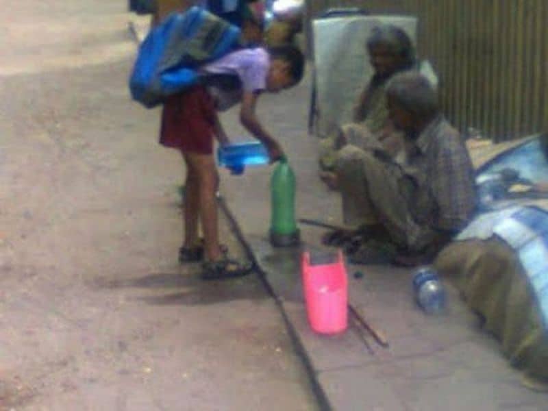 A school boy gives water to the thirsty homeless man