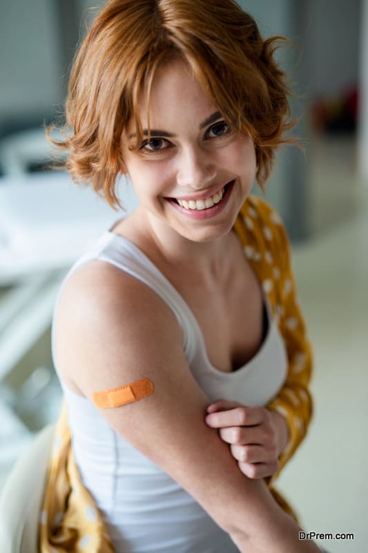 Portrait of happy woman with plaster on arm after vaccination in hospital, looking at camera