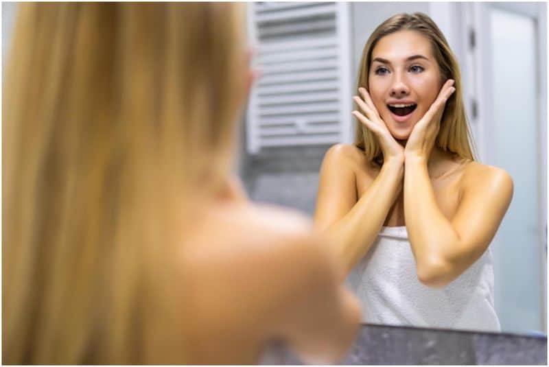 Happy woman looking at herself in the bathroom mirror
