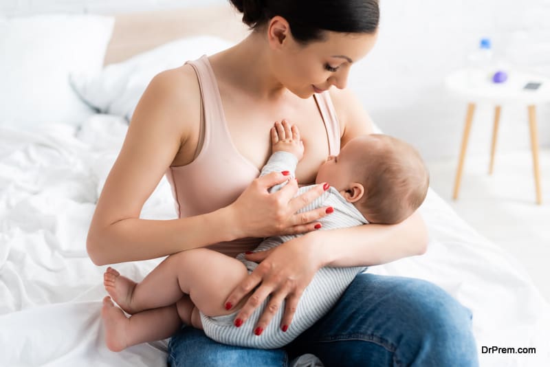 caring mother breastfeeding baby boy in bedroom