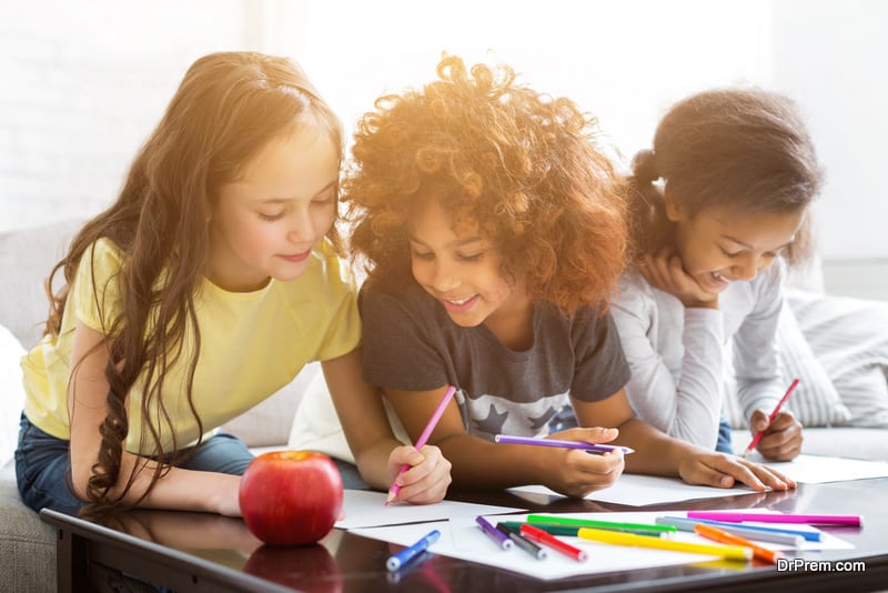 Multiethnic girls drawing at table with colorful pencils, spending time together