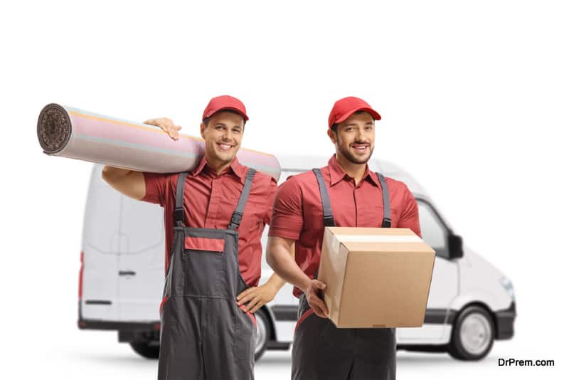 Workers from a moving company with a box and carpet in front of a white van isolated on white background