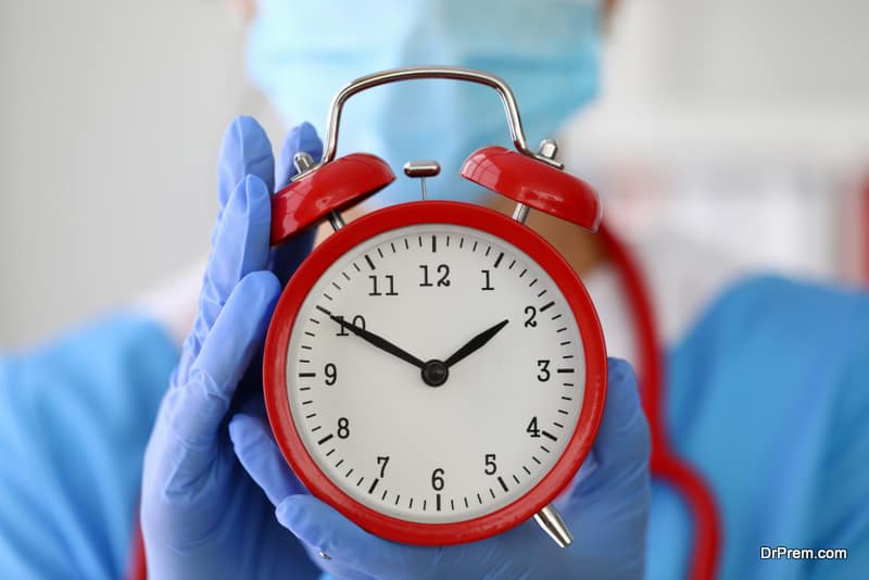 Doctor in gloves holds red alarm clock closeup. Features of the working hours of medical workers concept