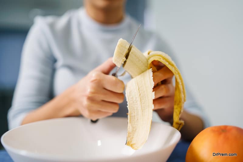 Caucasian woman sitting by the table at home cutting banana 