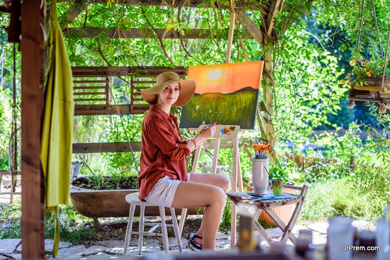 Young female artist working on her art canvas painting outdoors in her garden.