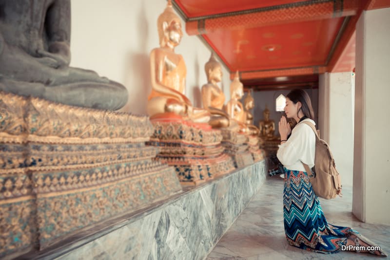 elegance smiling female tourist kneel down in Bangkok famous wat pho temple and praying with buddha with vintage retro film color style on Thailand travel