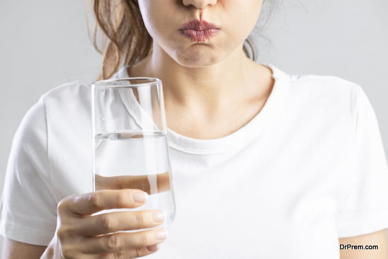 Young woman gargling while using mouthwash from a glass