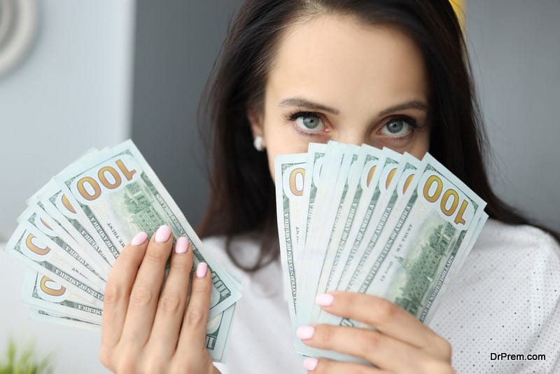 Woman holds one hundred dollar bills at face level and looks at camera
