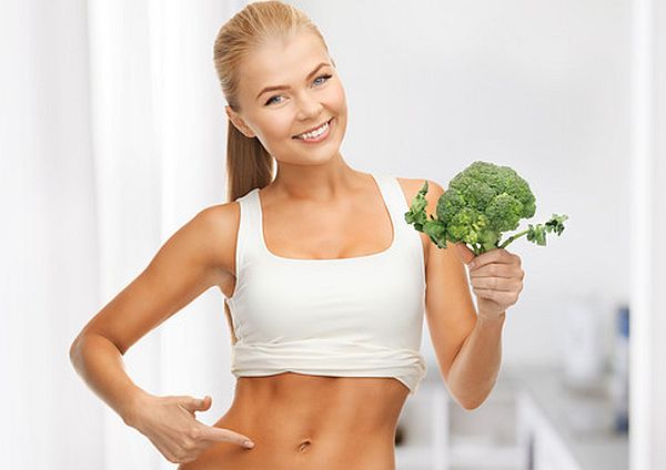 woman pointing at her abs and holding broccoli