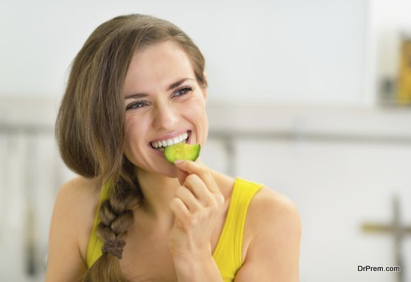 Portrait of young woman eating cucumber in kitchen