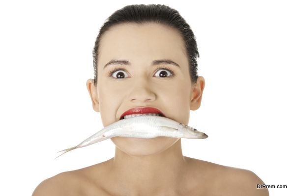 Beautiful young woman with fresh fish in her mouth, isolated on white background.