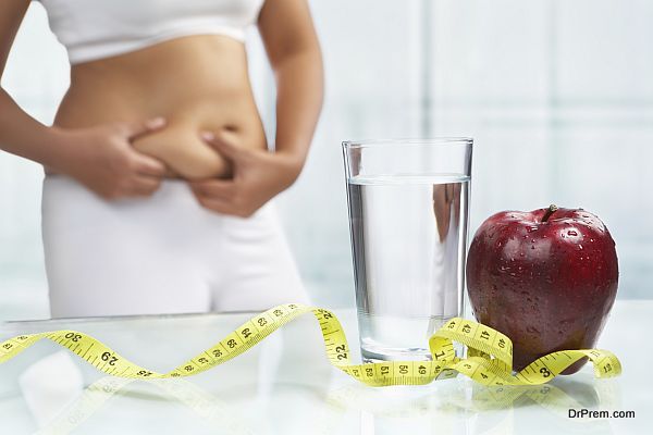 red apple and water with measuring tape on table with female body on sport attire at background for diet concept