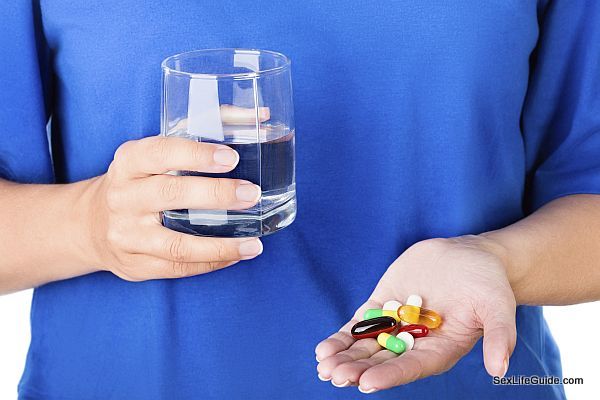 Female in blue t-shirt holding glass of water and pack of different colored pills