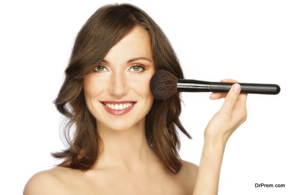 Beautiful happy smiling young woman applying make-up with big brush, on white background