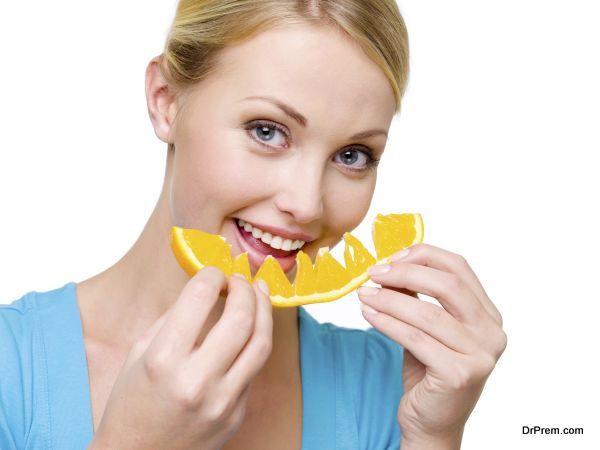 Attractive smiling woman eats the fresh orange - over white background