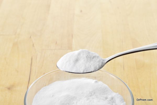 Close-up of baking soda on spoon against background of glass of water on wooden table. Bicarbonate of soda.