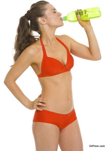 Young woman in swimsuit drinking from bottle of water