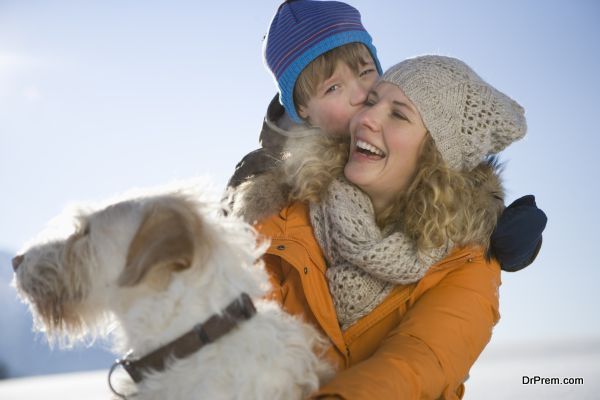 Mother laughing with son and pet dog in snow