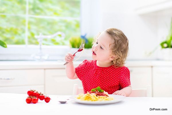 Sweet toddler girl eating spaghetti in white kitchen