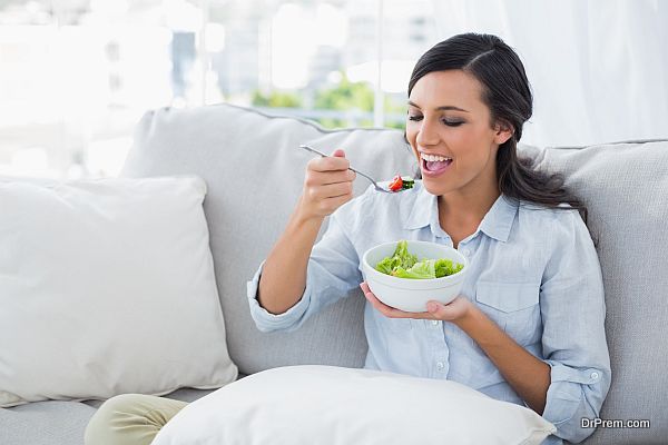 Happy woman relaxing on the sofa eating salad