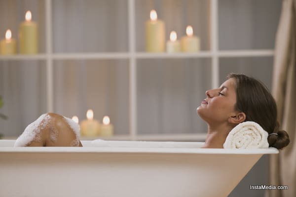 Content woman lying in bathtub with candles