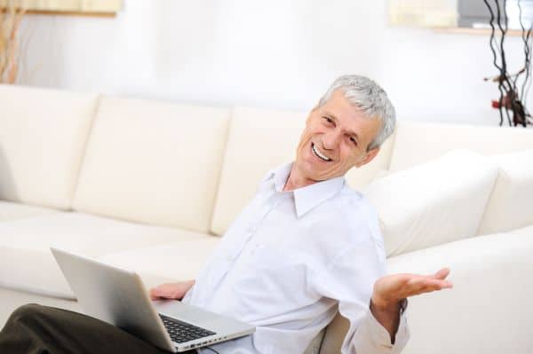 relaxed senior man with laptop on sofa smiling