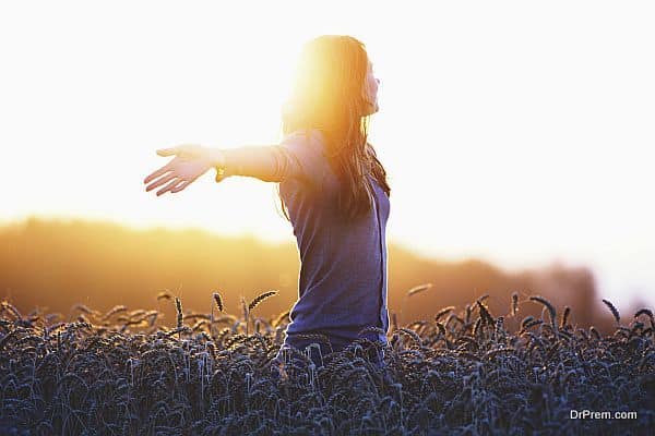 Young woman enjoying sunlight with raised arms in straw field