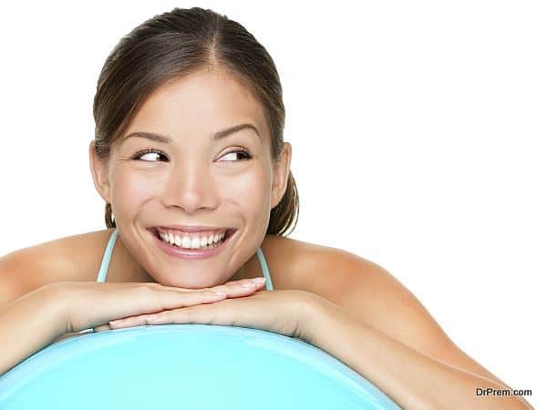 Gym pilates woman looking to the side showing something. Beautiful young healthy lifestyle woman relaxing on pilates exercise ball after workout.  Mixed race fitness model isolated on white background.