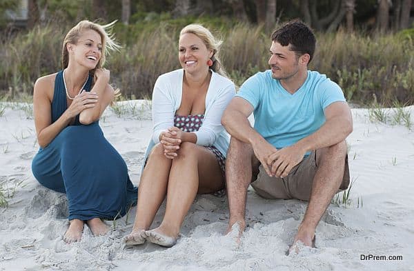 Three friends sit on the beach talking at sunset