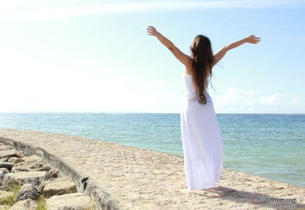 Woman relaxing at the beach with arms open enjoying her freedom wear long white dress