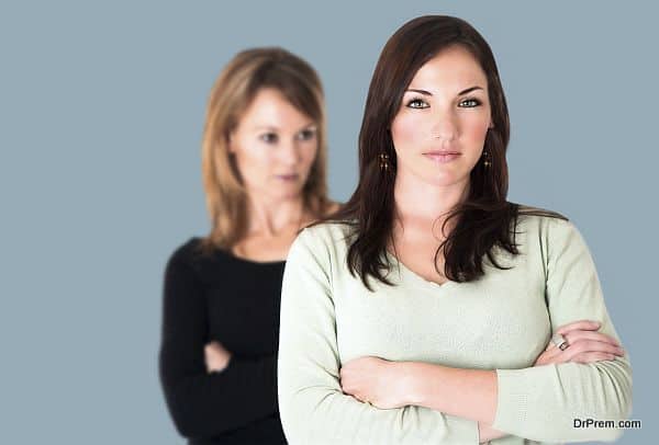 Confident young brunette with arms crossed and her jealous opponent in the background