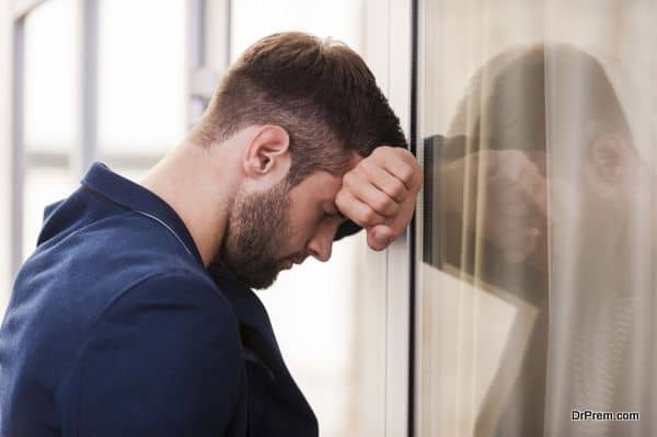 Tired and depressed. Frustrated young man in smart casual wear keeping eyes closed while standing indoors