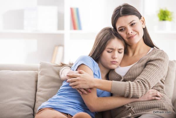 Mother and teen daughter are hugging after quarrel on sofa at home.