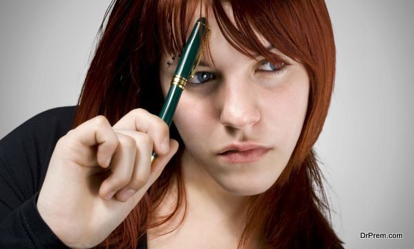 Cute girl with red hair holding a pen against her forehead and thinking.Studio shot.