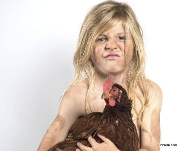Close up of a dirty child with scraggly hair holding a chicken against a light background