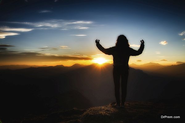 Girl in yoga meditation on top of a mountain at sunset