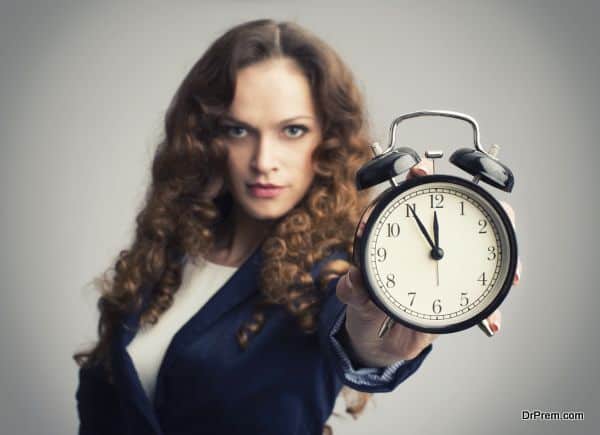 Girl showing alarm clock over gray background
