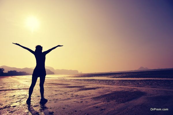 cheering young woman open arms on sunrise beach