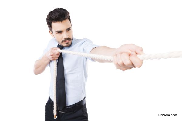 Everyday winner. Confident young man in shirt and tie pulling a rope while standing against white background