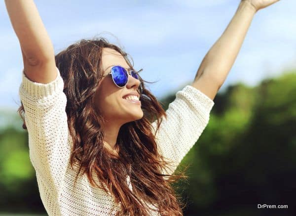 Attractive happy woman in sunglasses enjoying freedom outdoors with hand raised