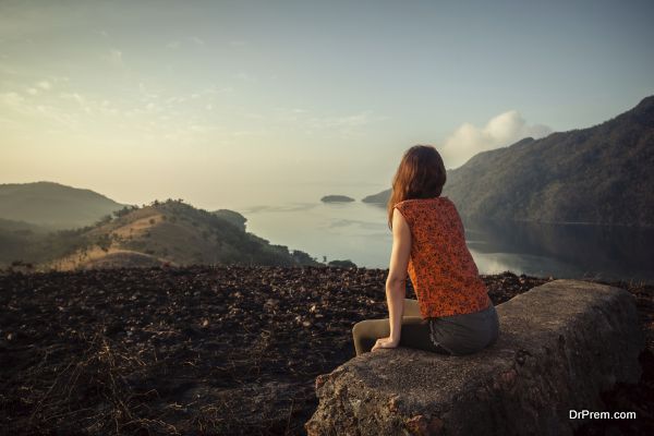 A young woman is sitting on an unusual rock on a mountain overlooking a bay at sunrise in a tropical climate