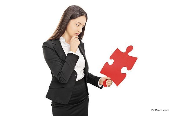 Young brunette businesswoman looking at a big red piece of a puzzle isolated on white background