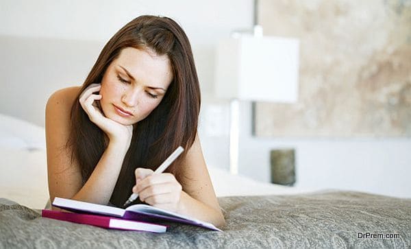 Young woman lying on a bed writing in a notebook